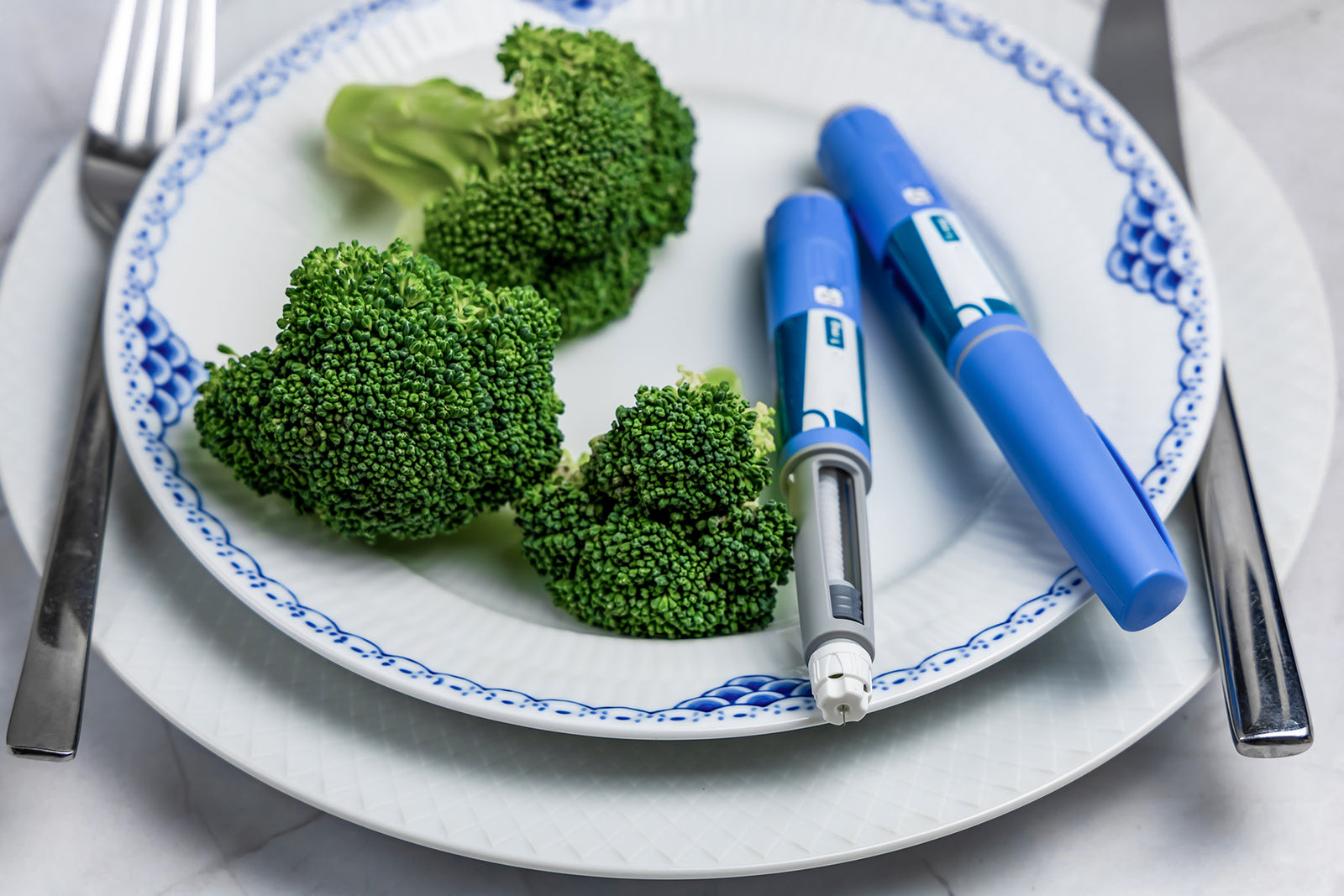Two Ozempic pens sitting on a plate with tree pieces of broccoli